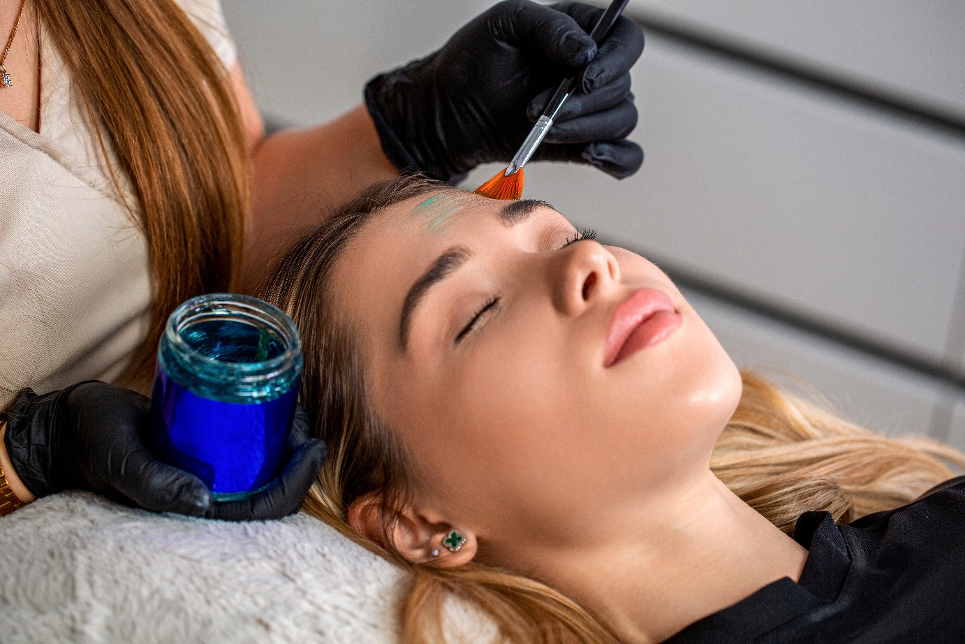 Doctor hand esthetician applying glycolic acid peel on face of young woman. Young woman getting a facial mask treatment at the beauty salon. Facial skin care procedures.
