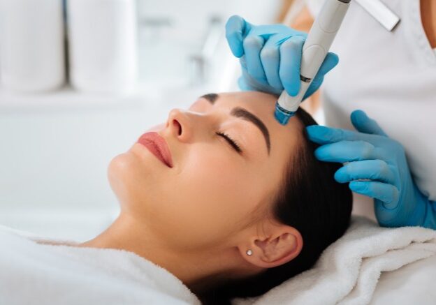 Professional cosmetology. Smart skilled cosmetologist using a modern device while doing hydrafacial procedure